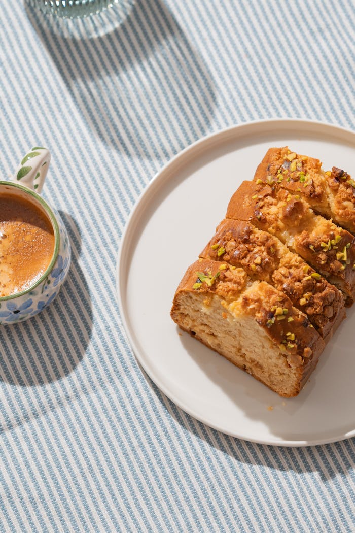 Warm breakfast setting with a slice of cake and a cup of coffee on a striped tablecloth.